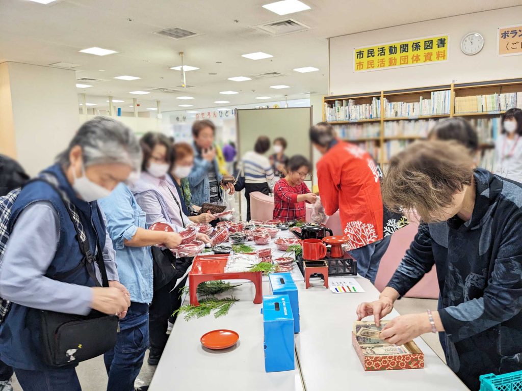 机におおぜいの人が集まる漆器の販売。手前に募金箱が２つある